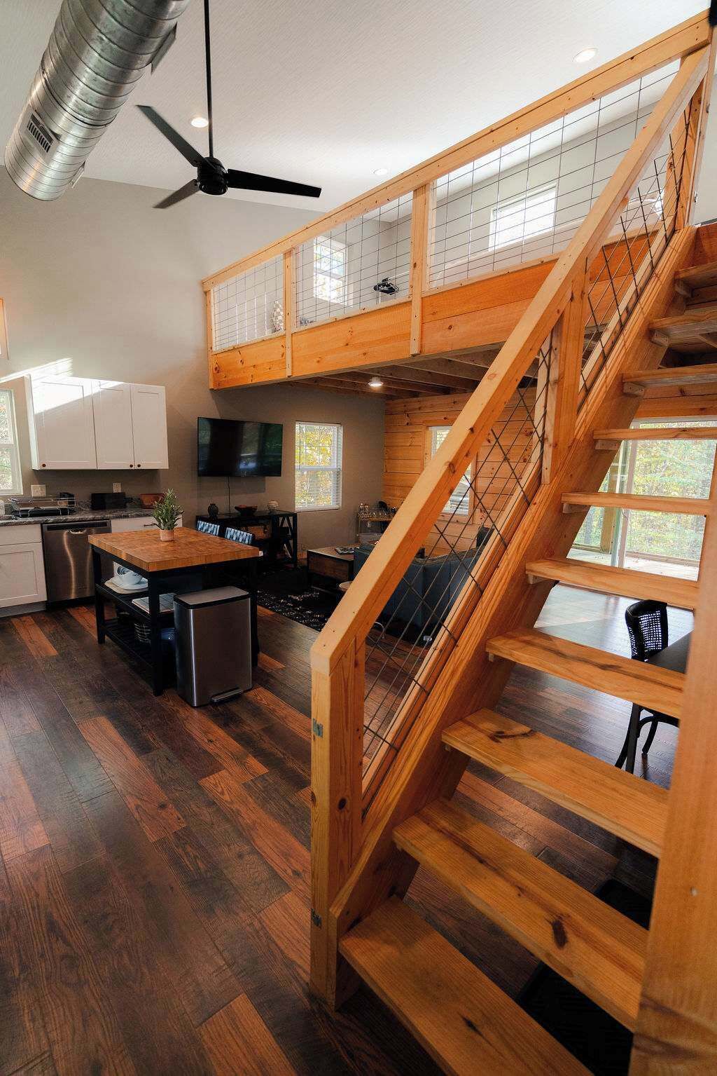 A spacious kitchen with modern appliances, a dining area with a wooden table, and a staircase with a glass railing leading to an upper level.