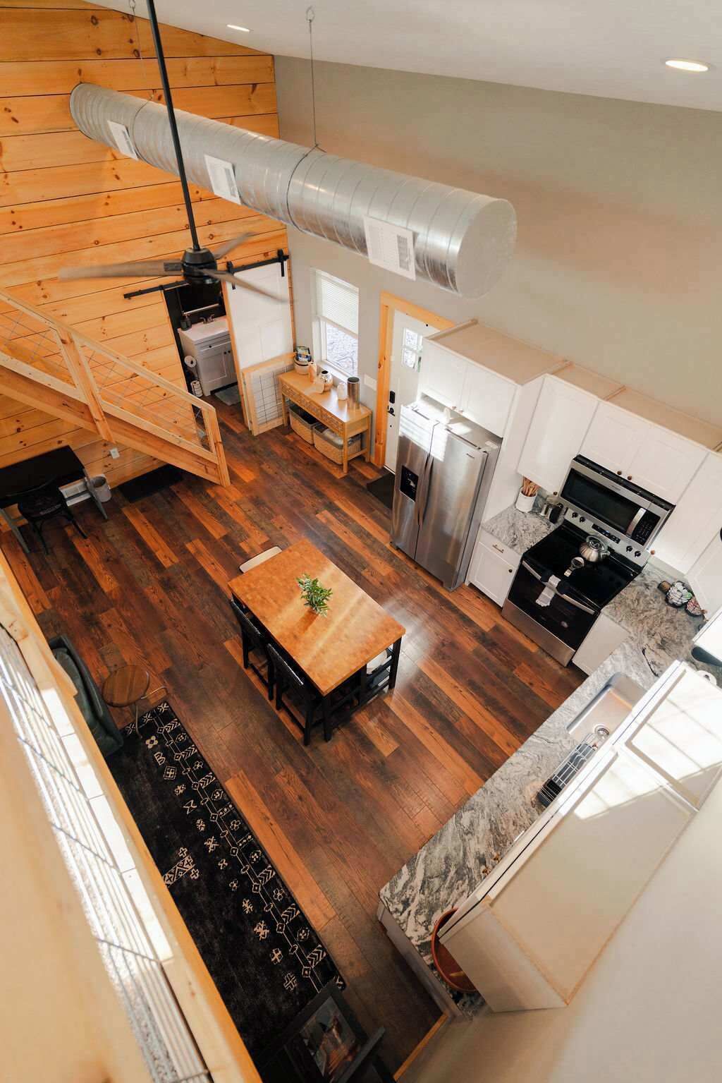 A modern kitchen with a central island, a dining area with a wooden table, and a staircase leading to an upper level.