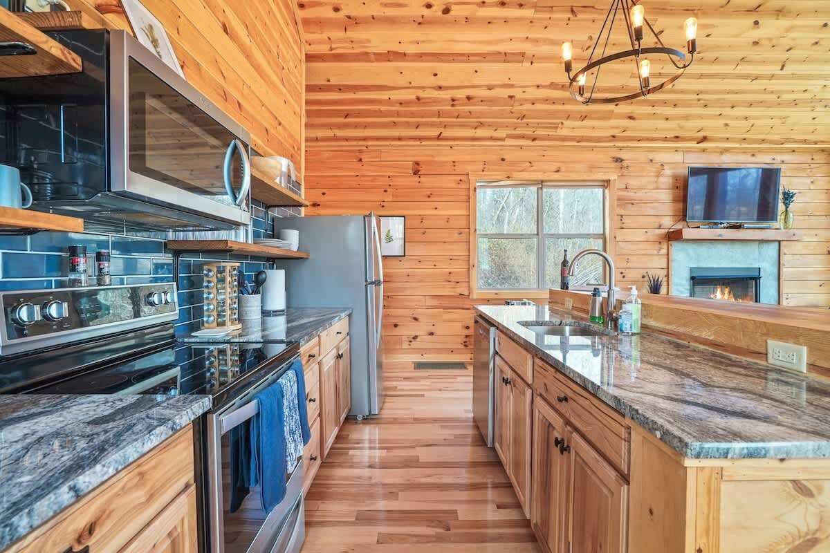 A modern kitchen with wooden walls, a central island, stainless steel appliances, and a built-in TV.