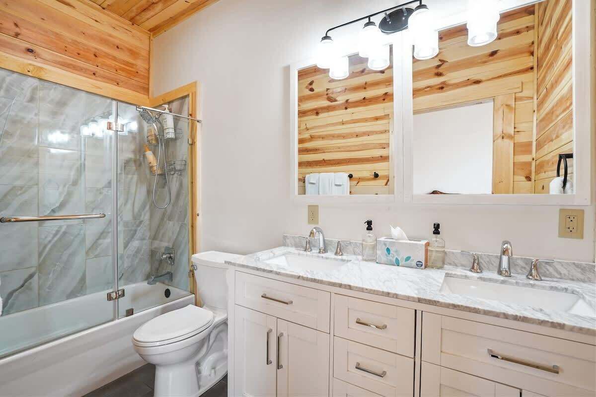 Un baño moderno con cabina de ducha de vidrio, inodoro blanco, lavamanos con encimera de mármol y muebles de madera.