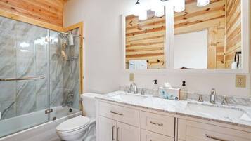 Un baño moderno con cabina de ducha de vidrio, inodoro blanco, lavamanos con encimera de mármol y muebles de madera.