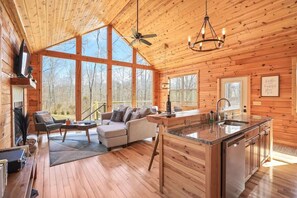 Una cabaña amplia con una sala de estar grande, una cocina con isla central y ventanas panorámicas con vistas al bosque.