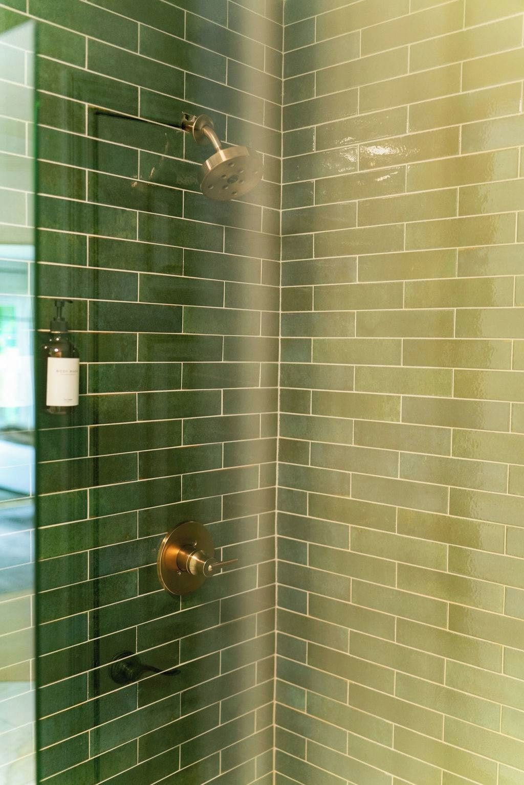 Un coin d’une pièce dont les murs sont recouverts de carreaux verts et qui comprend un espace douche.