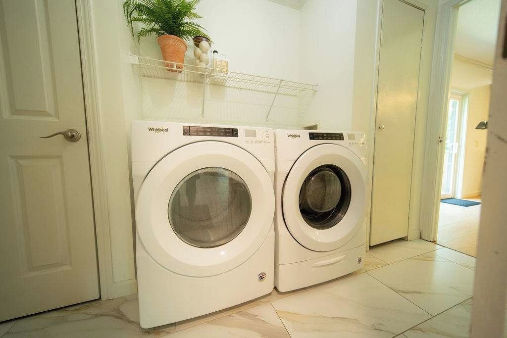 Two front-loading Whirlpool washing machines in a laundry room with a white door and a shelf above.