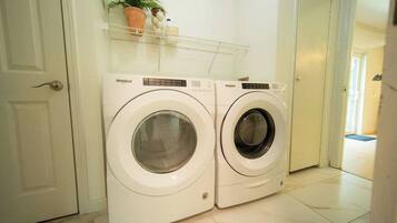 Two front-loading Whirlpool washing machines in a laundry room with a white door and a shelf above.