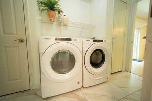 Two front-loading Whirlpool washing machines in a laundry room with a white door and a shelf above. - Buckingham Woods I Hocking Hills (Logan)