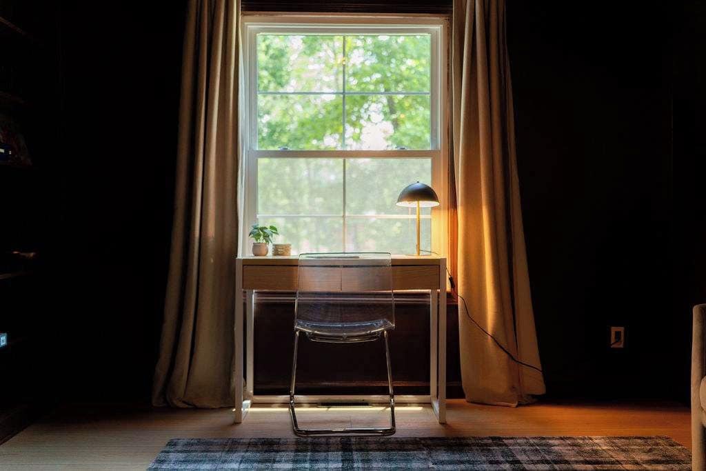 A room with a desk, a chair, a lamp, and a window with curtains.
