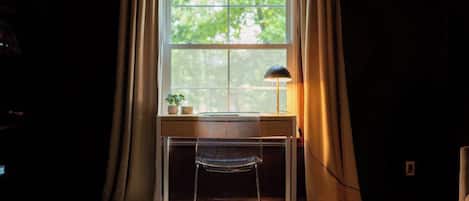 A room with a desk, a chair, a lamp, and a window with curtains.