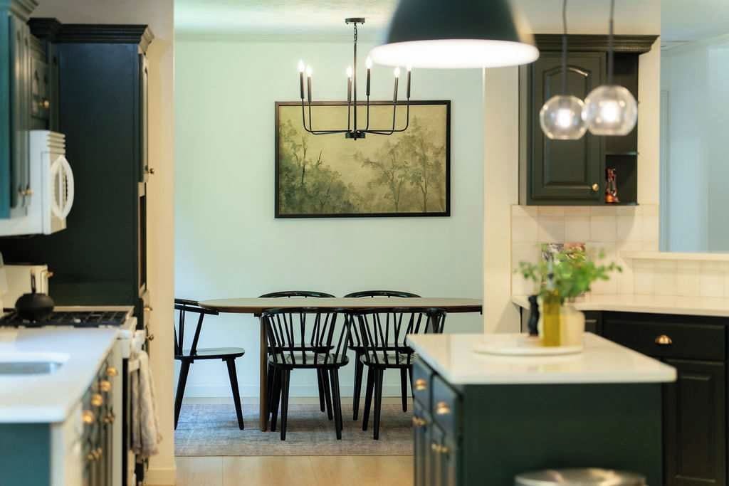 A kitchen with a dining table and chairs, a pendant light, and a framed artwork on the wall.