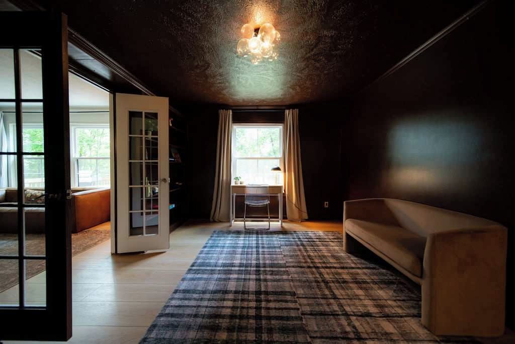 A room with a large window, a desk, a sofa, and a patterned rug.