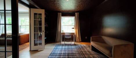 A room with a large window, a desk, a sofa, and a patterned rug.