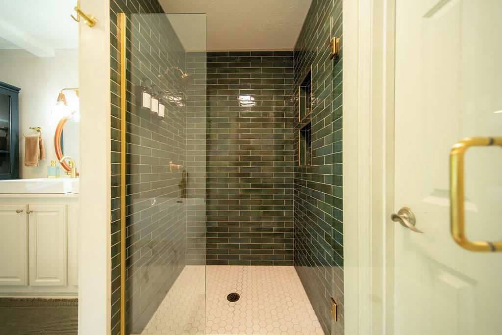 A glass-enclosed shower with a tiled floor, a white door with a gold handle, and a visible towel rack.