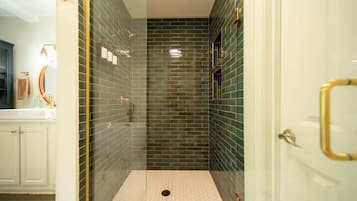 A glass-enclosed shower with a tiled floor, a white door with a gold handle, and a visible towel rack.