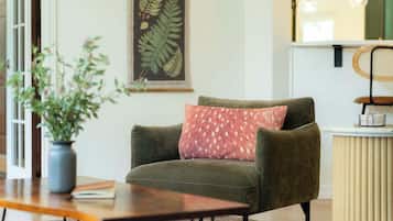 A room with a green armchair, a wooden table, a potted plant, and a wall-mounted artwork.