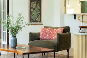 A room with a green armchair, a wooden table, a potted plant, and a wall-mounted artwork. - Buckingham Woods I Hocking Hills (Logan)