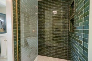 Een badkamer met donkergroene mozaïektegels, een glazen douchecabine en een wit wastafelgedeelte.