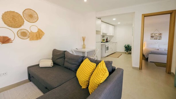 Een moderne woonkamer met een grijze bank, gele sierkussens en decoratieve wandversieringen.