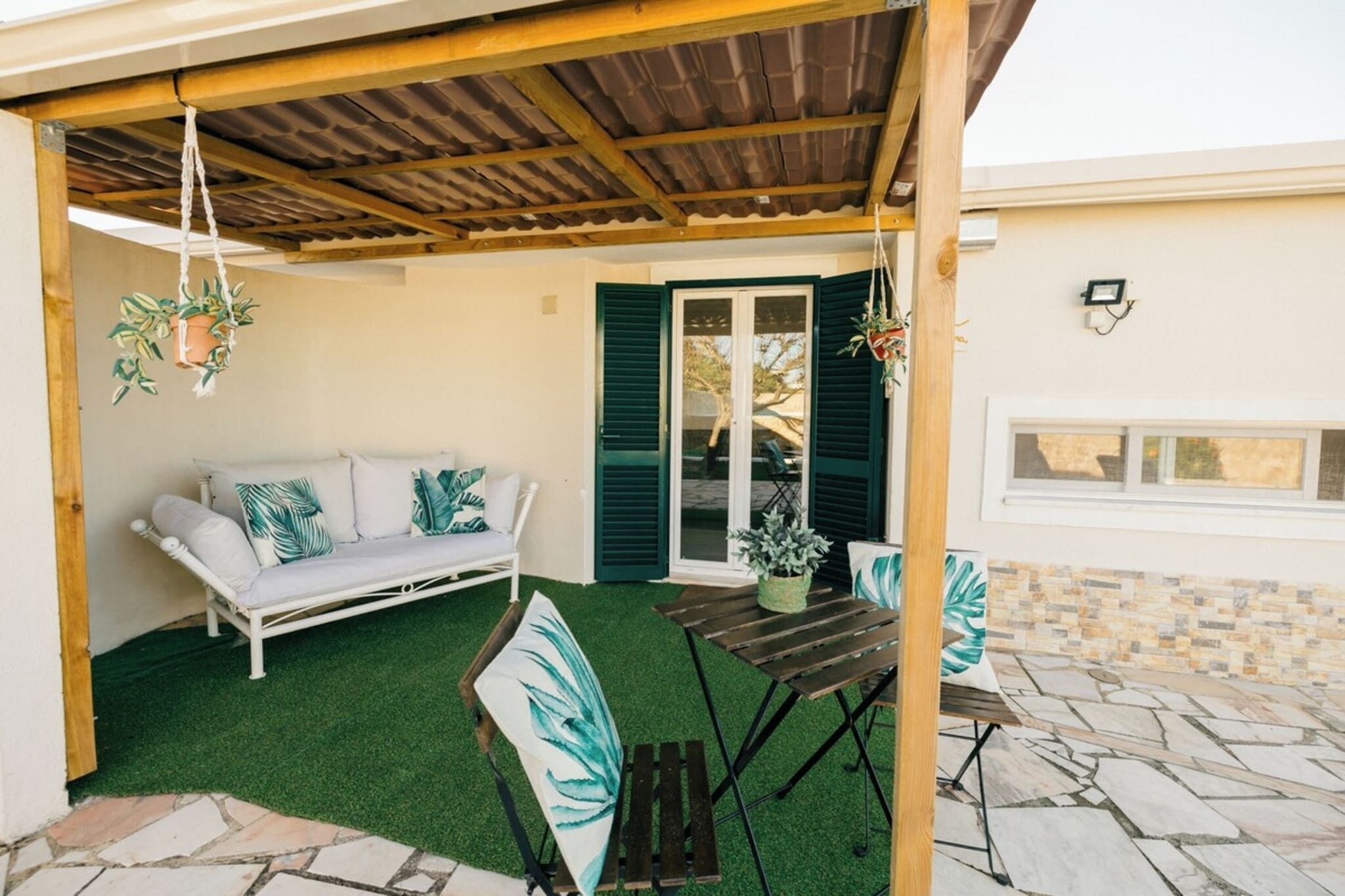 En overdækket terrasse med en hvid sofa, et træbord og krukker med planter.