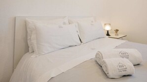 A neatly made bed with white linens and pillows, a bedside lamp, and two towels with a logo on them.