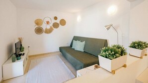 A minimalist bedroom with a green sofa, a white bedside table with a lamp, and decorative wall art.