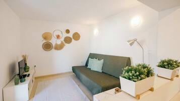 Et minimalistisk soveværelse med en grøn sofa, et hvidt natbord med lampe, og dekorativ vægkunst.
