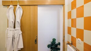 A bathroom with a wooden door, a potted plant, and a towel rack with two white towels.