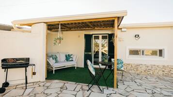 Una zona patio esterna con pavimento in pietra, un barbecue, un divano bianco con cuscini, un tavolino e una pianta pensile.