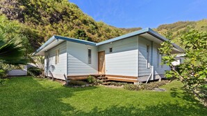 Une maison à deux étages avec un porche à l’avant, entourée d’une pelouse bien entretenue et adossée à une colline.