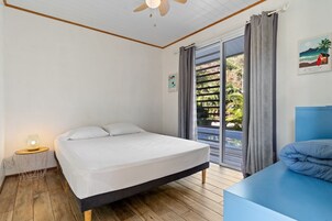 Un dormitorio con cama, mesita de noche, ventilador de techo, ventana con cortinas y vistas al exterior.
