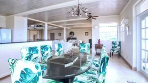 A spacious dining area with a round glass table surrounded by chairs with a tropical leaf pattern. - Landsdown House - by Zenbreak (Oistins)