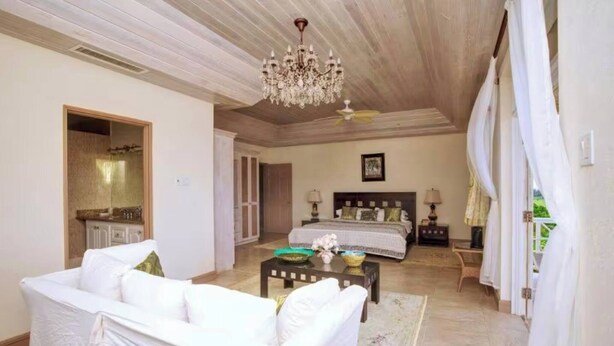 A spacious bedroom with a large bed, a chandelier, a ceiling fan, and a view of the outdoors. - Landsdown House - by Zenbreak (Oistins)