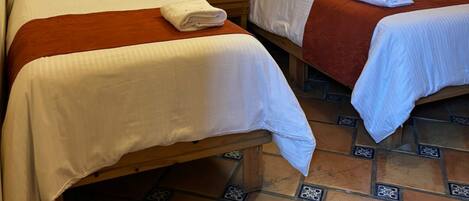 Two single beds with wooden headboards, white linens, and brown throw blankets.