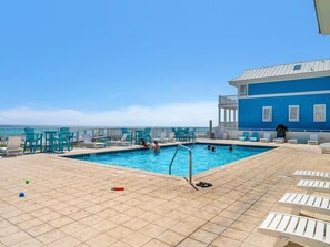 A pool area with a view of the ocean, lounge chairs, and a building with a blue facade.