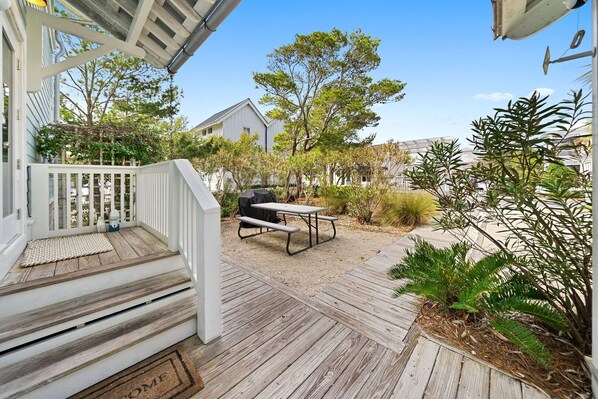 A wooden deck with a picnic table and grill, surrounded by various plants and trees.