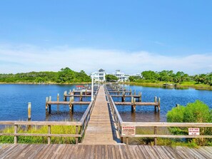 A wooden pier leading to a white building with a dock extending into a lake, surrounded by greenery.