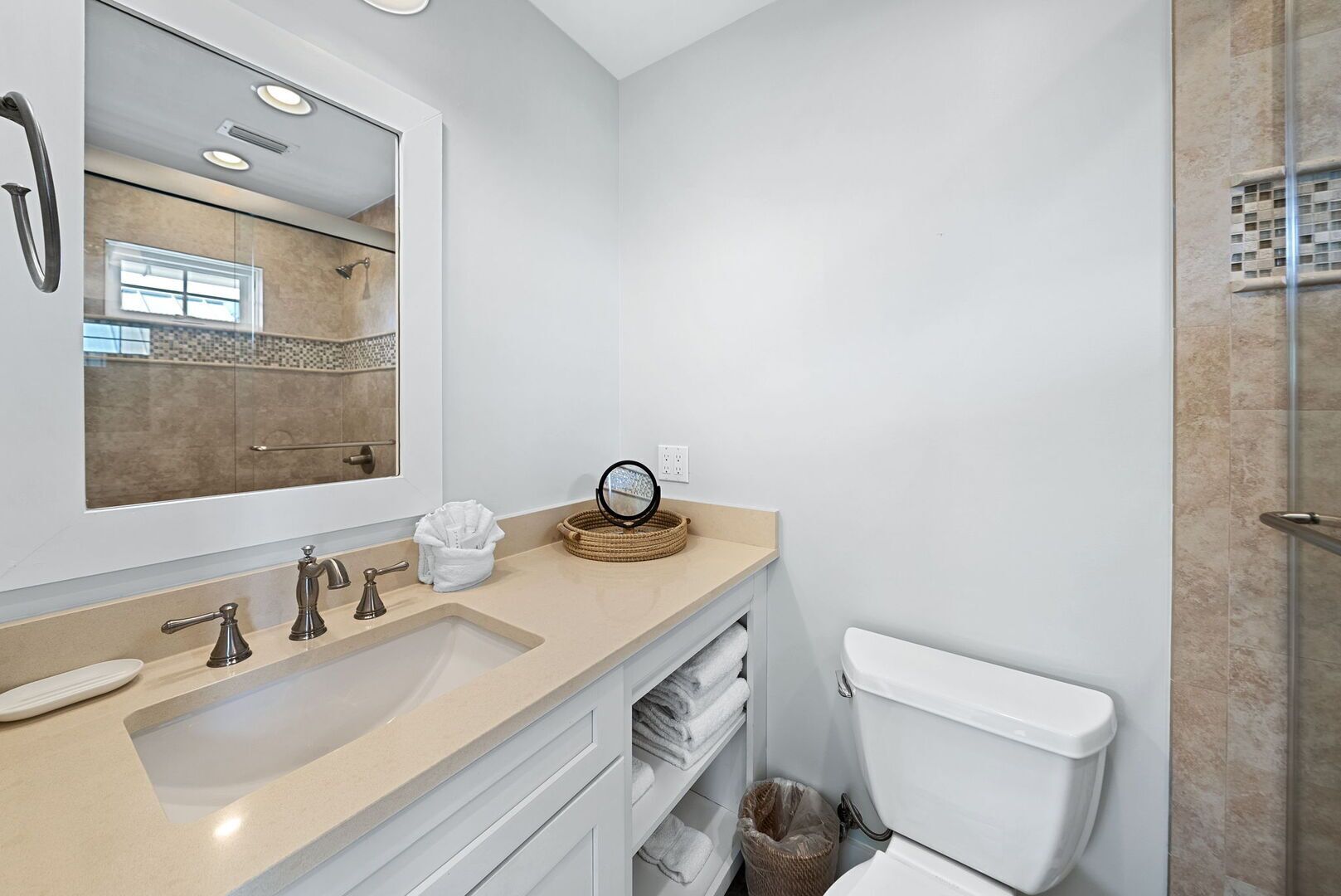 Un baño moderno con un espejo grande, una encimera color beige, un lavabo, un inodoro y una zona de ducha.