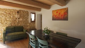 Un espace repas agrémenté d’un mur en pierre, de poutres en bois au plafond, d’un canapé vert et d’une table avec des chaises.