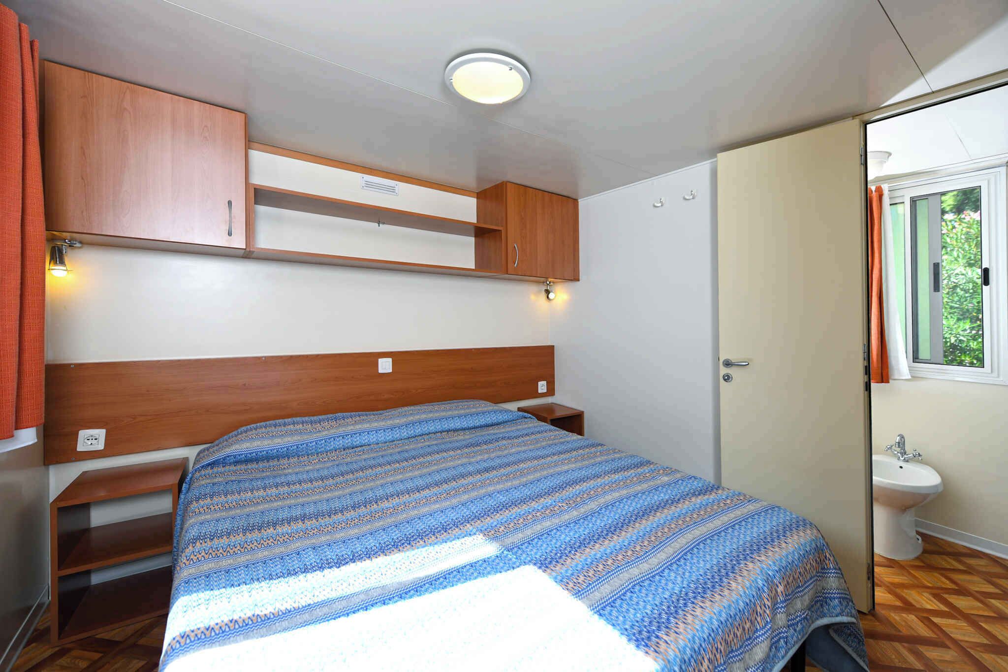 Ein kleines Schlafzimmer mit einem Einzelbett, einem Holz-Kopfteil, einer eingebauten Ablage, einem Nachttisch und einem Fenster mit Vorhängen.