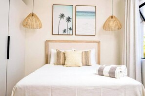 A neatly made bed with a white bedspread and two pillows, two framed pictures above the bed, and two wicker pendant lights. - Azzurro #9 - by Zenbreak (Holetown)