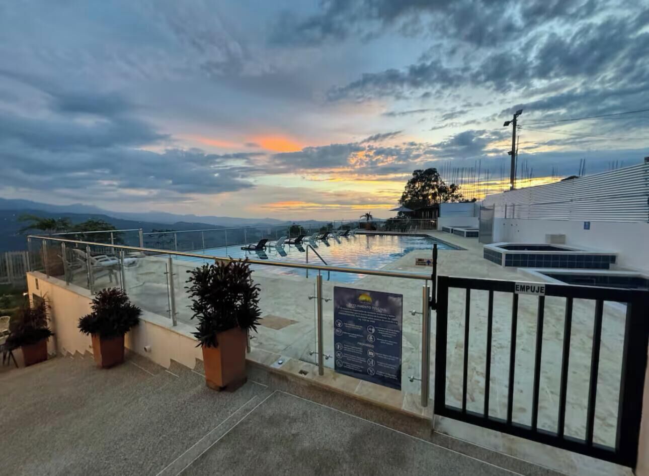A rooftop terrace with potted plants, a gated entrance, and a view of the sunset over the cityscape.