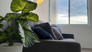 Una sala de estar moderna con un sofá gris, una mesa de centro blanca y una planta grande verde en una maceta blanca.