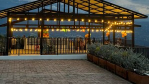 Un espacio al aire libre techado con estructura de madera, luces colgantes y vistas del paisaje.