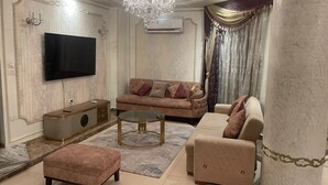 A spacious living room with a large flat-screen TV, a chandelier, and a sofa set.