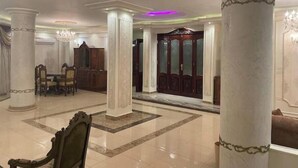 A spacious lobby with marble flooring, large columns, a grand chandelier, and a wooden cabinet.