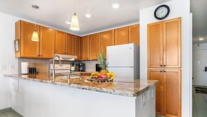 A modern kitchen with wooden cabinets, a granite countertop, and a central island. - Spectacular Oceanfront Views - Wifi - Free Concierge - Vrkcv (Kailua-Kona)