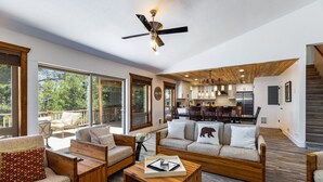 A spacious living area with a ceiling fan, large windows, a wooden coffee table, and a cozy seating arrangement.