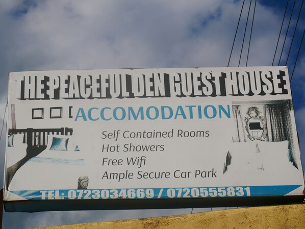 A sign for The Peaceful Guest House, highlighting features like self-contained rooms, hot showers, free wifi, and an ample secure car park.