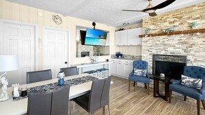 A modern living room with a fireplace, a flat-screen TV, and a dining area with a table and chairs. - Admiral's Quarter: Cozy 2-bedroom, beachfront condo with stunning sunset view (Wells)