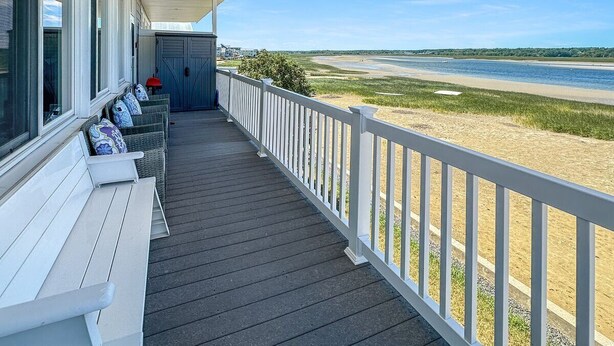 A covered porch with white railings, a bench, and a row of wicker chairs with cushions. - Admiral's Quarter: Cozy 2-bedroom, beachfront condo with stunning sunset view (Wells)