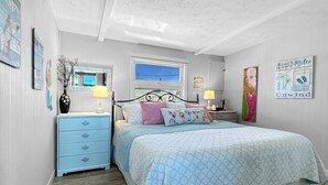 A bedroom with a bed, a nightstand, a dresser, a window, and wall art. - Admiral's Quarter: Cozy 2-bedroom, beachfront condo with stunning sunset view (Wells)